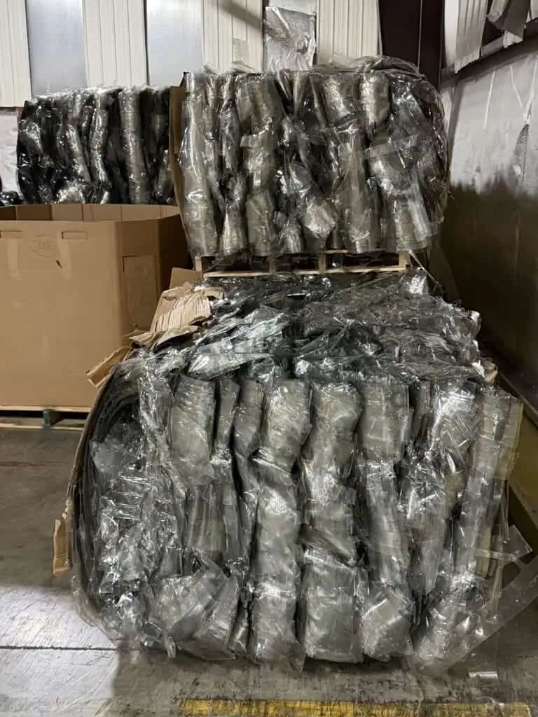 Pallets stacked with metal components wrapped in clear plastic inside a warehouse.
